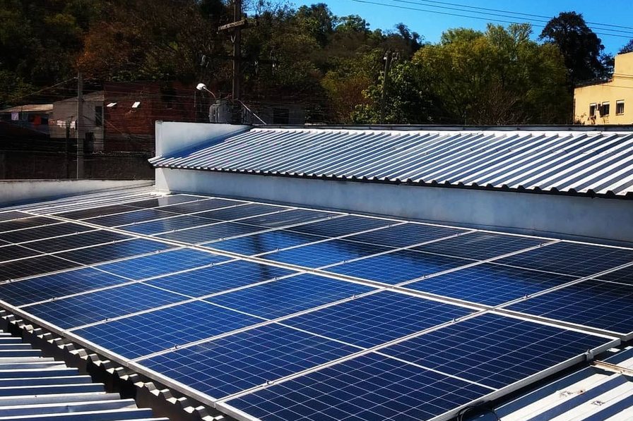 Instalação sobre telhado de zinco, com encosta arborizada e rede elétrica ao fundo.