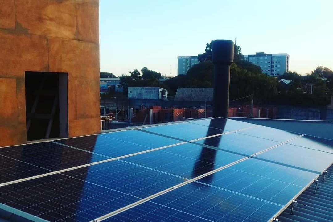 Módulos fotovoltaicos instalados sobre um telhado, com uma parede de reboco cor de telha ao lado.